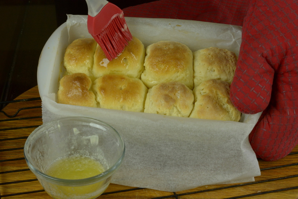The final brushing of melted butter on soft dinner rolls while still warm.