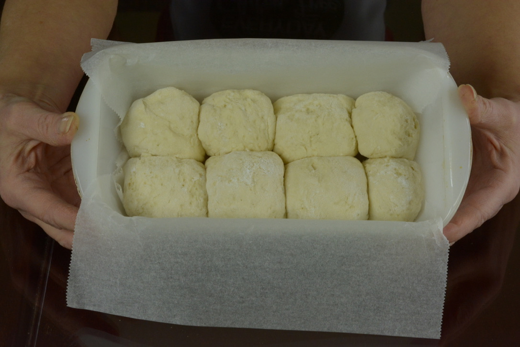 Soft dinner rolls rising in a loaf pan.