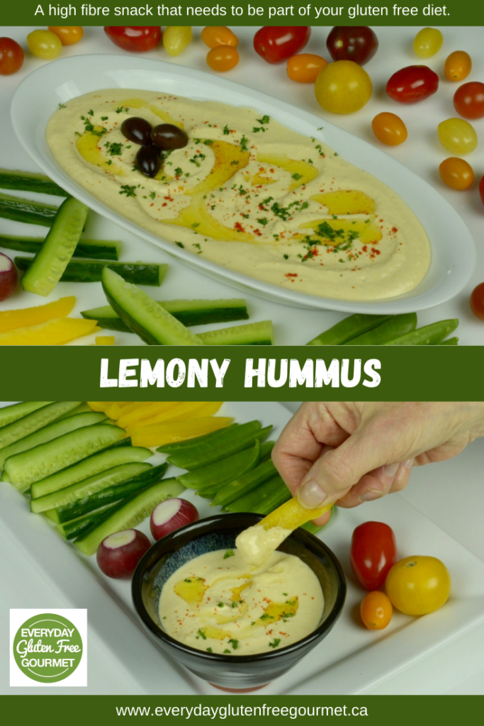 A dish of Lemony Hummus surrounded by raw vegetables and an individual serving with a hand dipping a piece of yellow pepper into it.