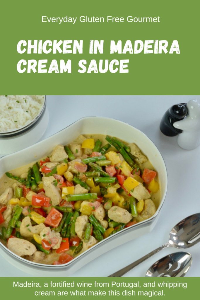 A white serving dish filled with Chicken in Madeira Cream Sauce with asparagus, red and yellow peppers.