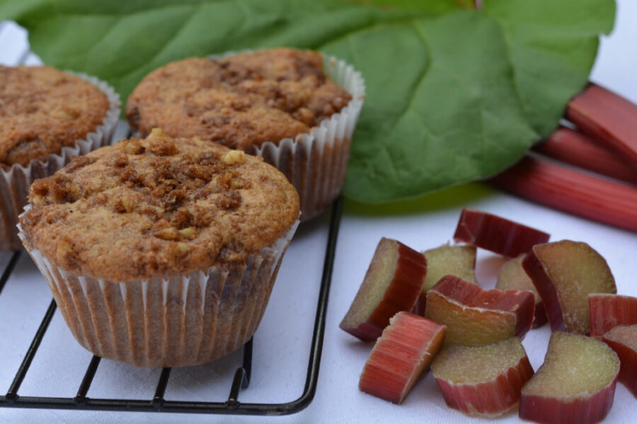 A baking rack with rhubarb streusel muffins surrounded by chopped rhubarb and a rhubarb leaf