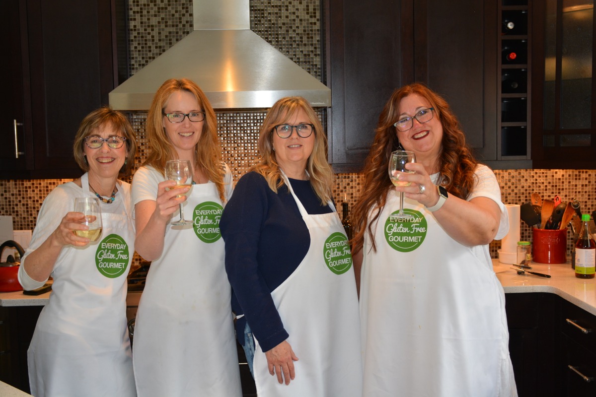 4 ladies wearing aprons in the Everyday Gluten Free Gourmet kitchen raising a glass to the first in person class in 2 years.
