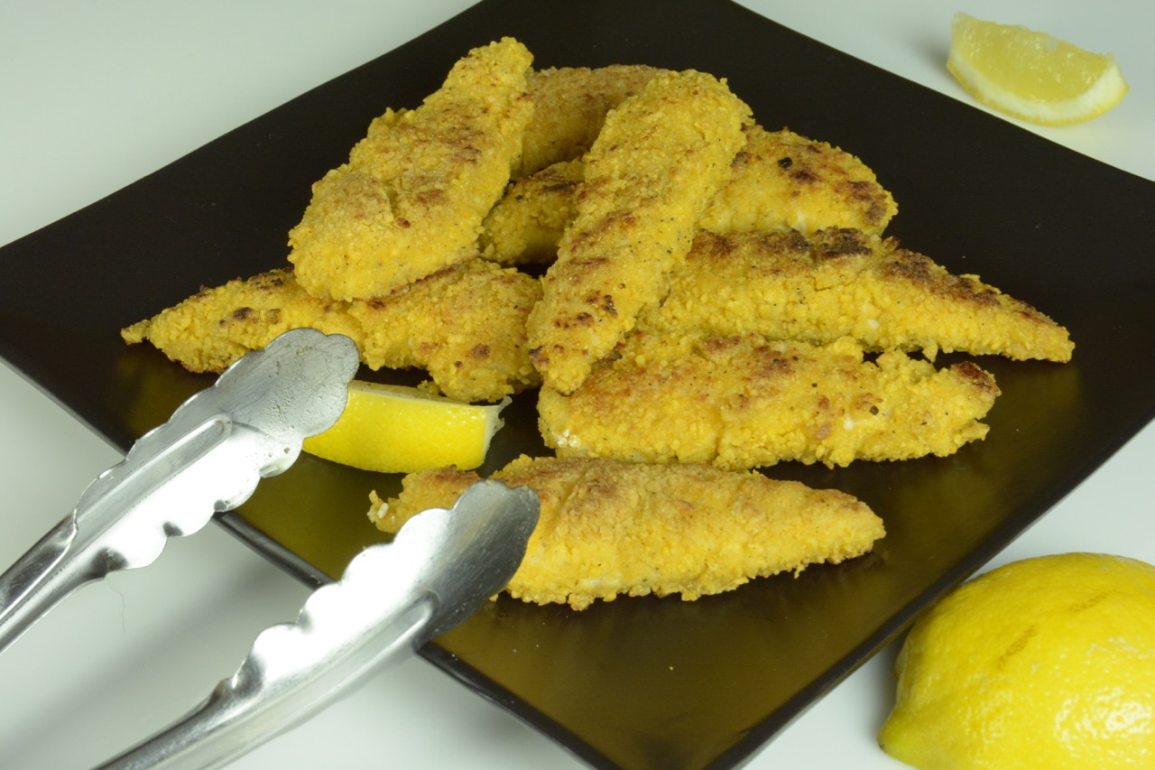 A black plate with breaded chicken strips and lemon wedges ready to serve.