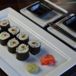 A white plate with futomaki, homemade sushi rolls, with pickled ginger and wasabi.