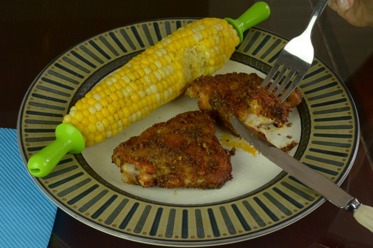 A dinner plate with two cooked chicken thighs with adobo paste and corn on the cob, each with a bite missing.