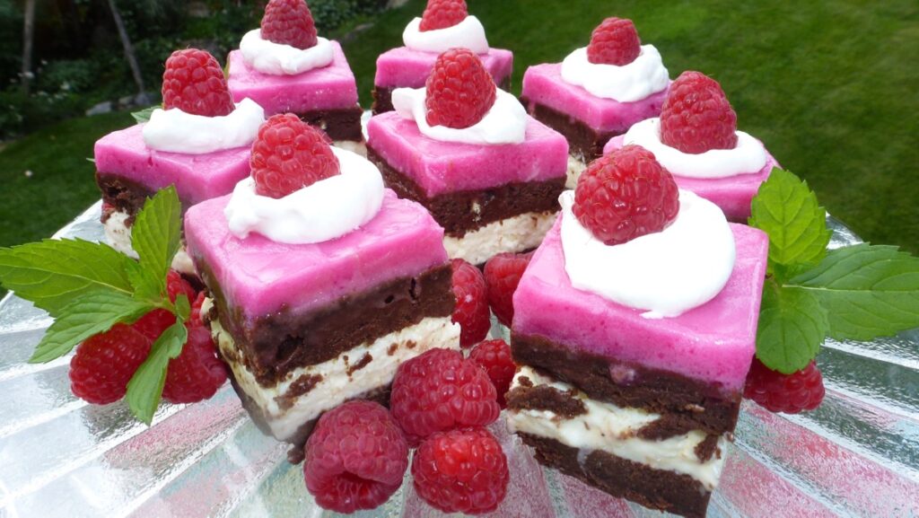 A pedestal tray with square pieces of a layered raspberry brownie ice cream cake.