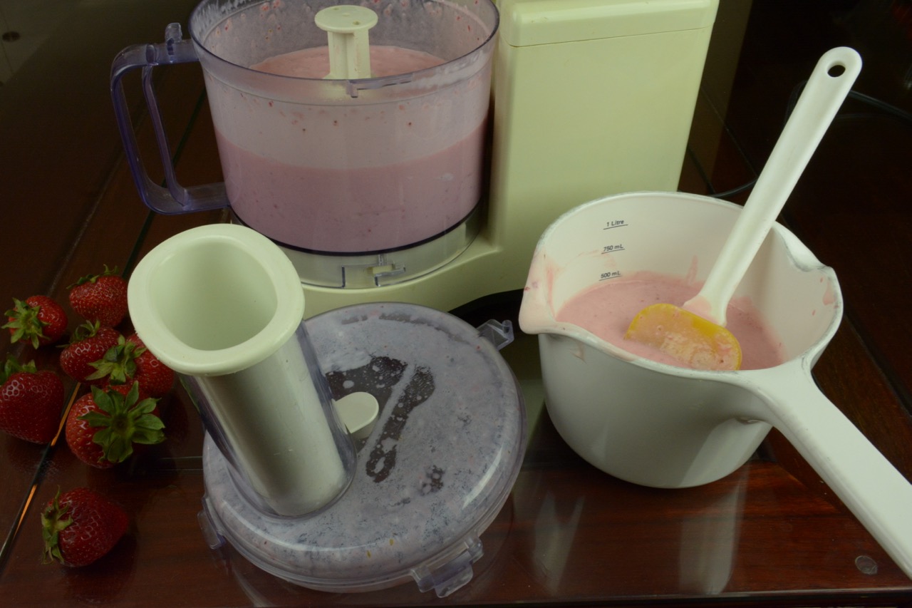 Pureed ingredients for Strawberry Cheesecake Ice Cream in a food processor with whole strawberries beside it.