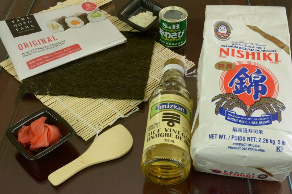 A bag of sushi rice, a bottle of rice vinegar, a tin of wasabi powder and sheets of nori, all gluten free.