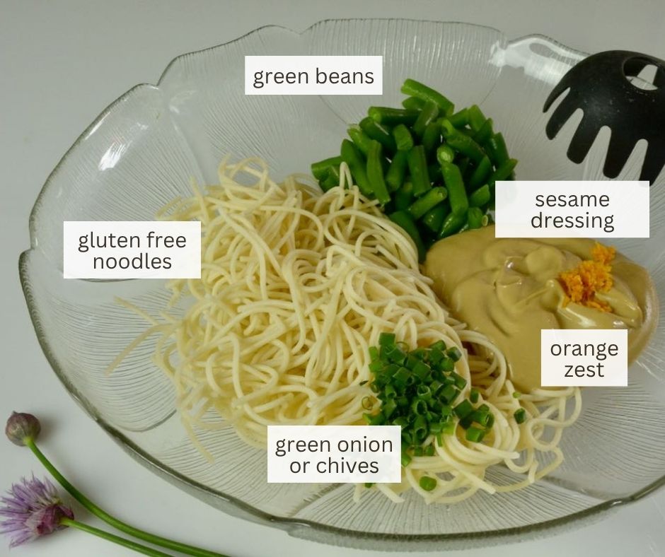 A bowl with ingredients; gluten free noodles, green beans, sesame mayonnaise dressing, orange zest and chives.