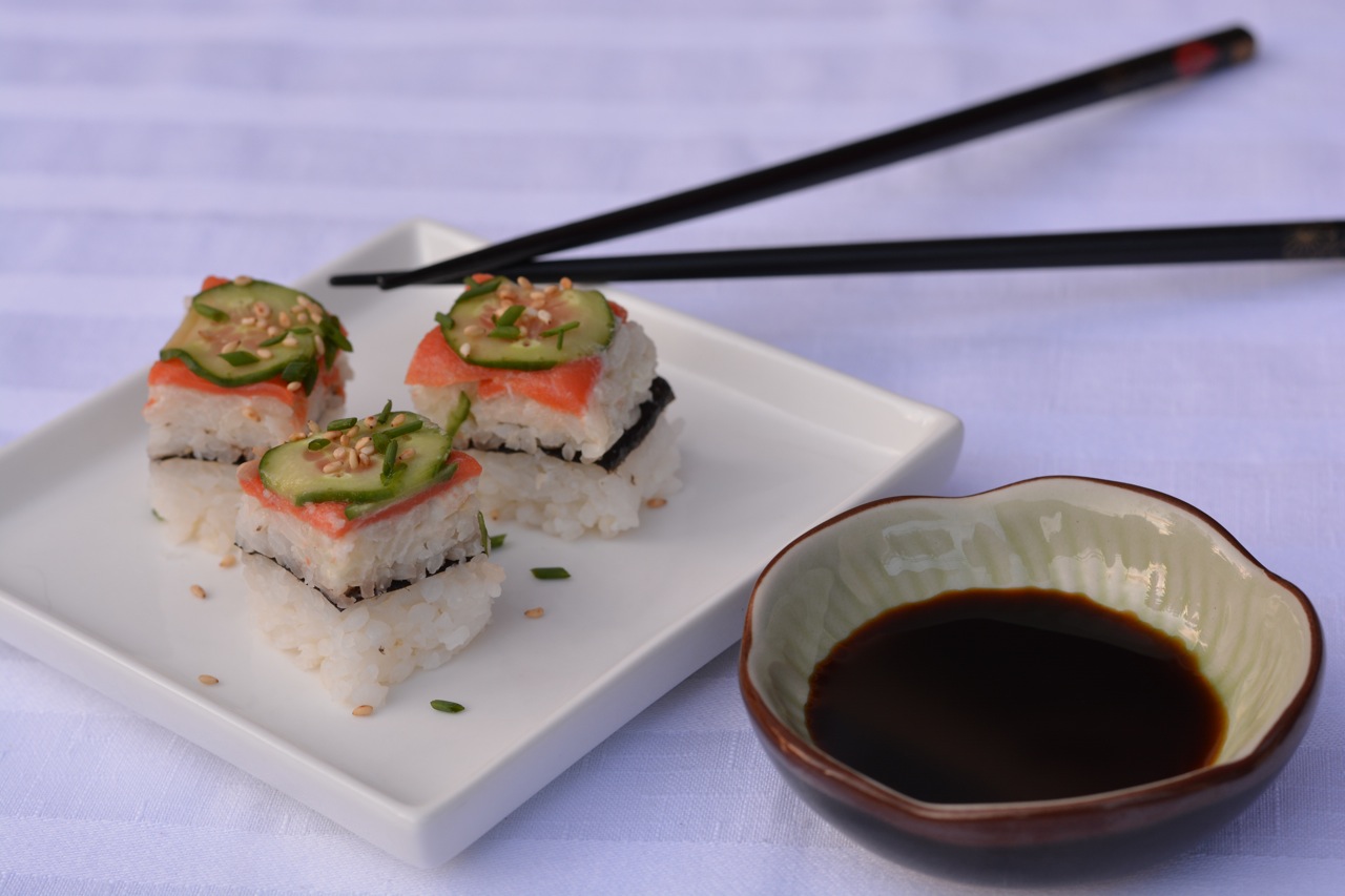 A plate of smoked salmon sushi pizza cut in squares and sprinkled with snipped chives and sesame seeds.