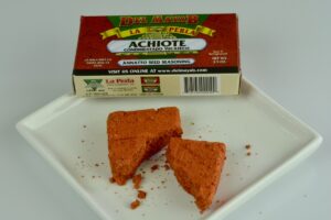 The box of achiote paste with the rust coloured brick, broken in half on a plate.
