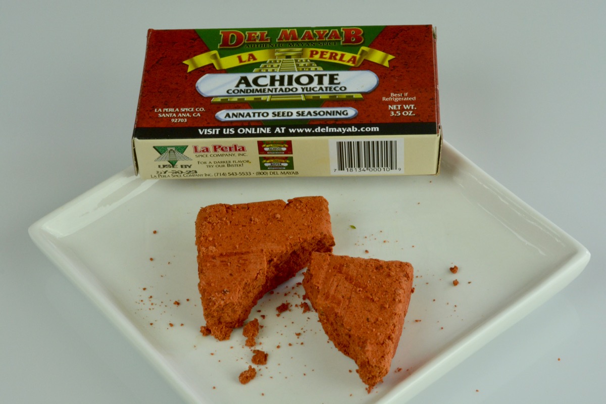 A small rust coloured brick of achiote paste in front of the box it came out of.