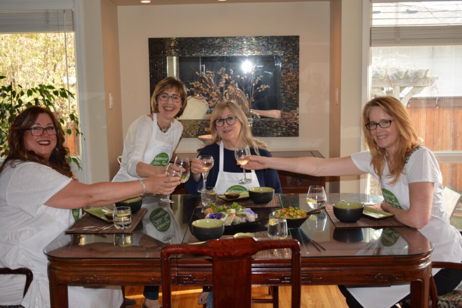 Four people at a dinner table raising their wine glasses to cheer for the Thai dinner they made.