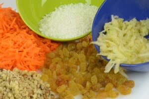 Bowls with grated carrot and apple, coconut, golden raisins and chopped walnuts.