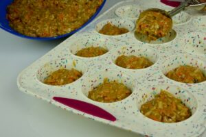 A silicone muffin pan with batter for Morning Glory muffins in the pan and a metal portion scoop ready to drop batter into another spot.