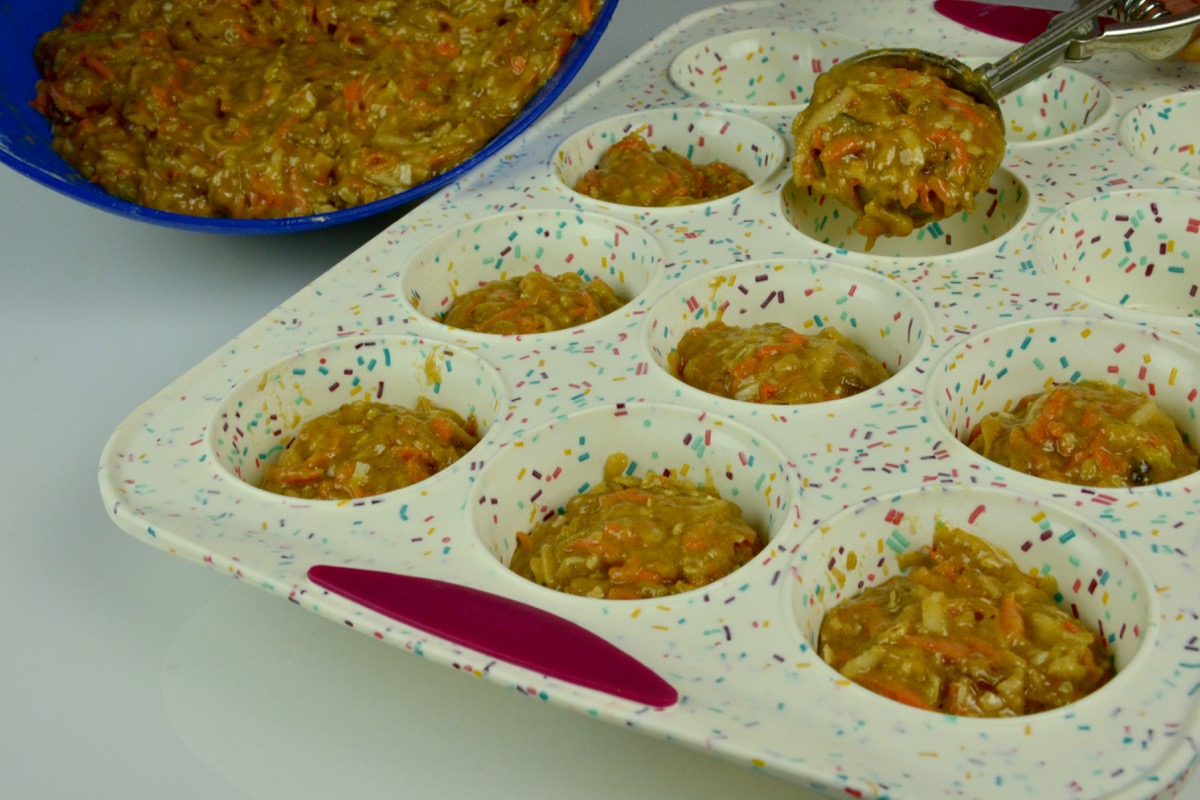 A silicone muffin pan with batter for gluten free Morning Glory muffins being scooped into it.