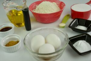 Muffin ingredients in cups and bowls; eggs, flour, sugar, oil, baking soda, xanthan gum, cinnamon and vanilla.