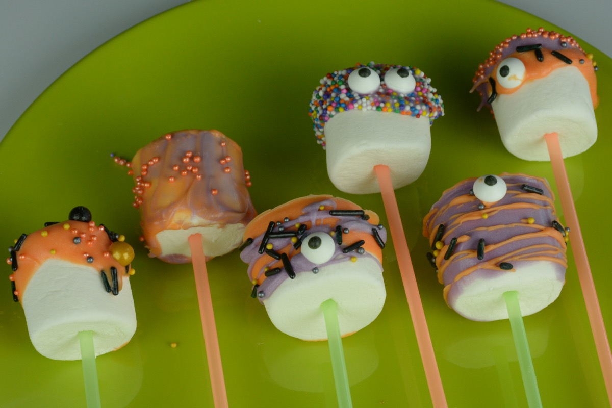 A green plate with marshmallows on a straw that have been dipped in coloured chocolate, Halloween sprinkles and a few googly eyes.
