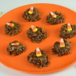 An orange plate of chocolate Uncooked Dainties each with an orange and yellow candy corn on top.