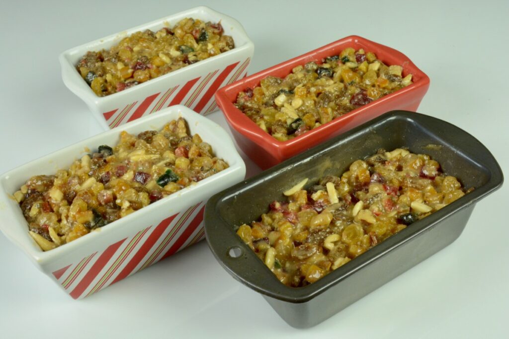 Four mini loaf pans filled with fruitcake batter.