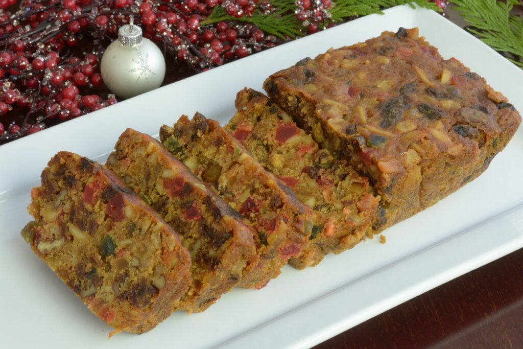 A white tray with slices of Light Christmas Fruitcake surrounded by holiday greenery and berries.