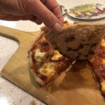A hand holding up one piece of a gluten free pizza showing the nice dark bottom of the crust.