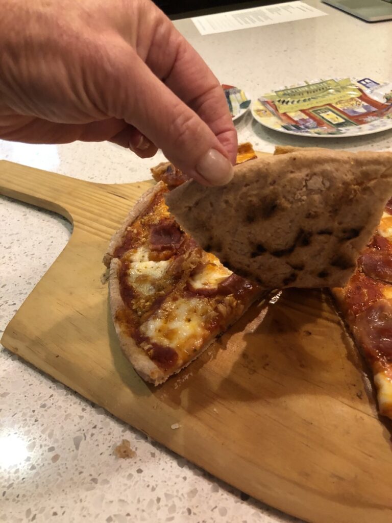 A hand holding up one piece of a gluten free pizza showing the nice dark bottom of the crust.