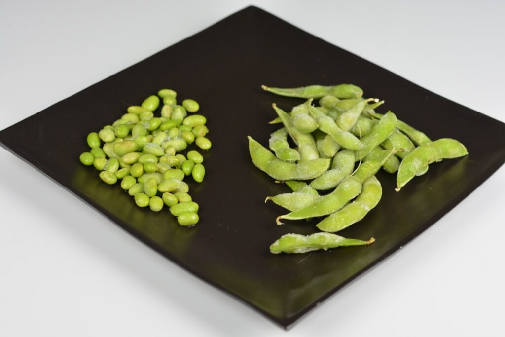 A black plate with frozen edamame beans shelled and in their pods for an easy edamame bean snack.
