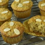 A baking rack with Banana Muffins each topped with 3 pieces of sliced almonds.