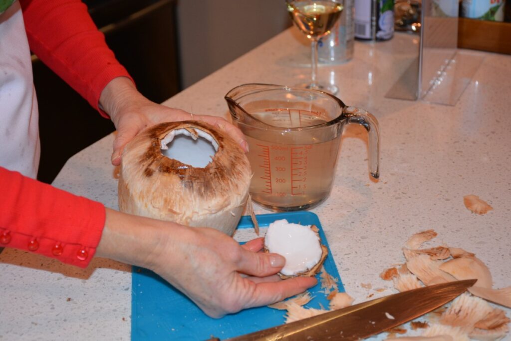 A young coconut with the top off and a cup of coconut water beside it to make coconut ice cream.