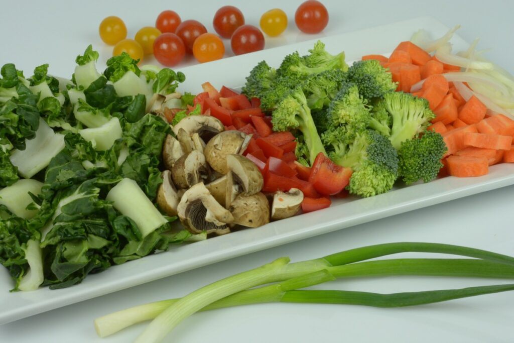 A tray of chopped bok choy, mushrooms, red pepper, broccoli, onion, carrot and cherry tomatoes ready to stir fry.