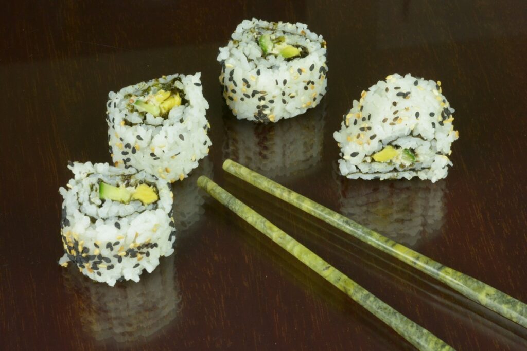 California rolls covered in black and brown sesame seeds on a dark table with a pair of jade chopsticks.