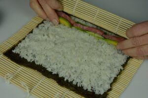 A bamboo mat with a sheet of nori topped with rice, tuna and avocado ready to be rolled into futomaki.
