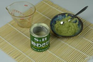 A bamboo mat with a dish of prepared wasabi paste and the can that the wasabi powder came from.