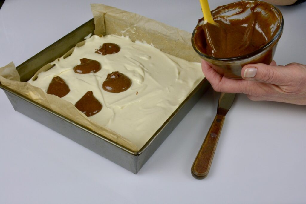 Adding blobs of the chocolate mixture on top of the cheesecake layer to make Chocolate Cheesecake Brownies.