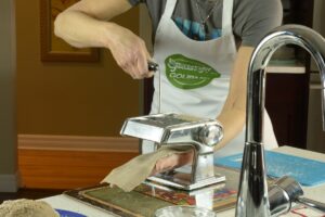 Rolling gluten free pasta dough through a hand crank machine.