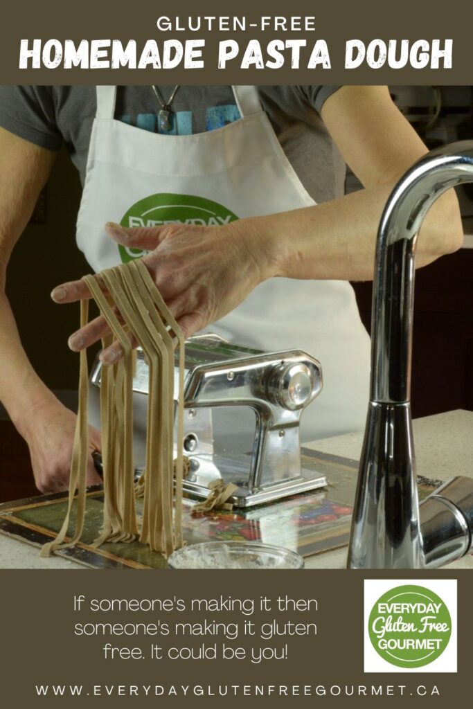 A hand full of homemade gluten free pasta cut into fettuccini, just coming out of a hand crank pasta machine.
