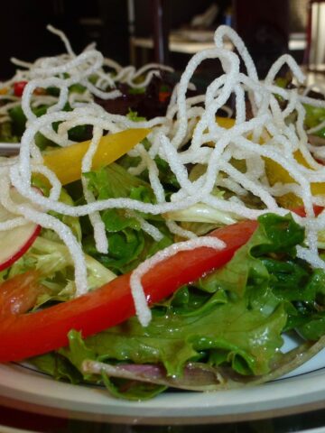 A plate of garden greens with Asian Dressing garnished with Crispy Bean Thread Noodles.