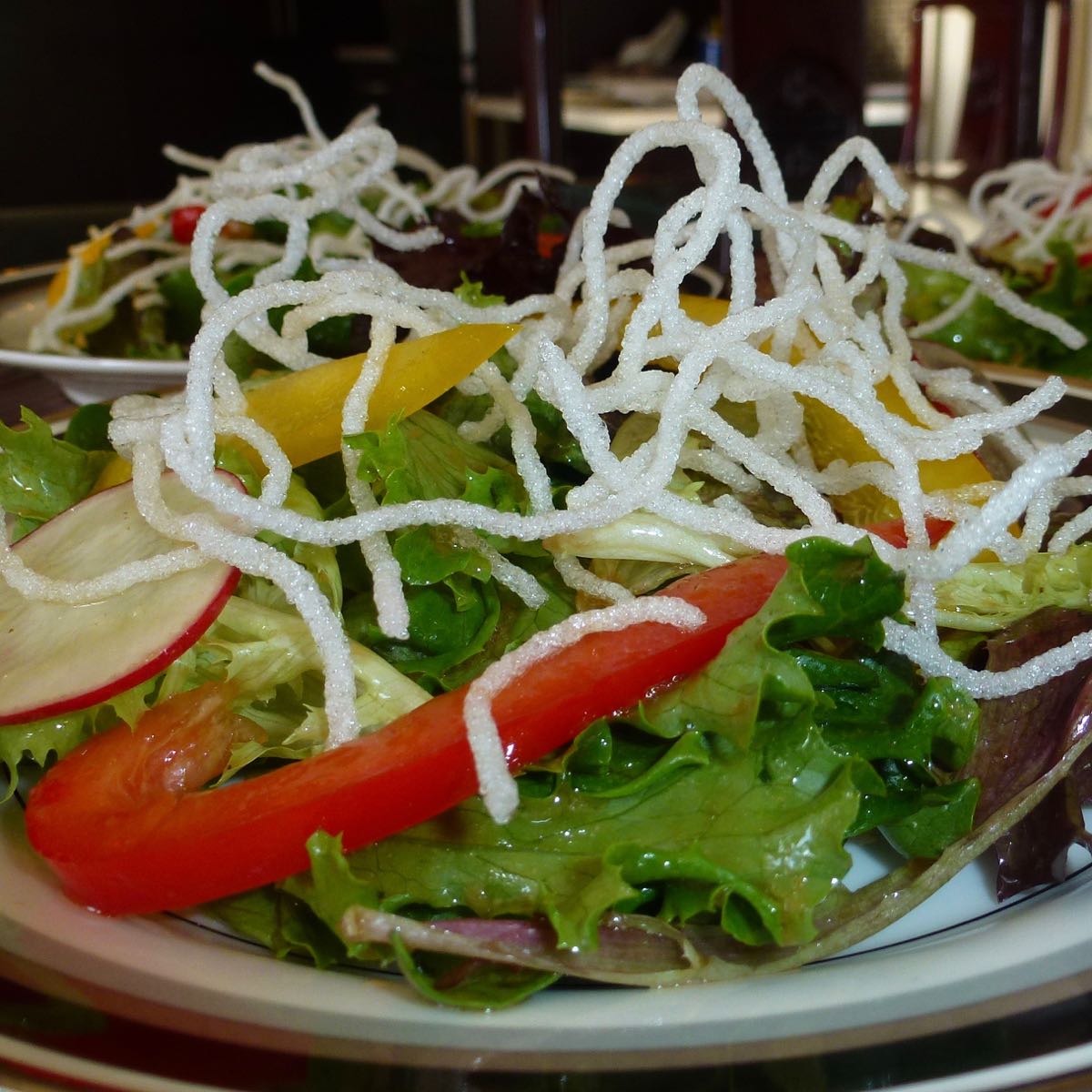 A plate of garden greens with Asian Dressing garnished with Crispy Bean Thread Noodles.