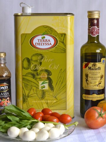 A bottle of Balsamic Glaze vs Balsamic Vinegar surrounded by fresh tomatoes, basil, bocconcini and olive oil.