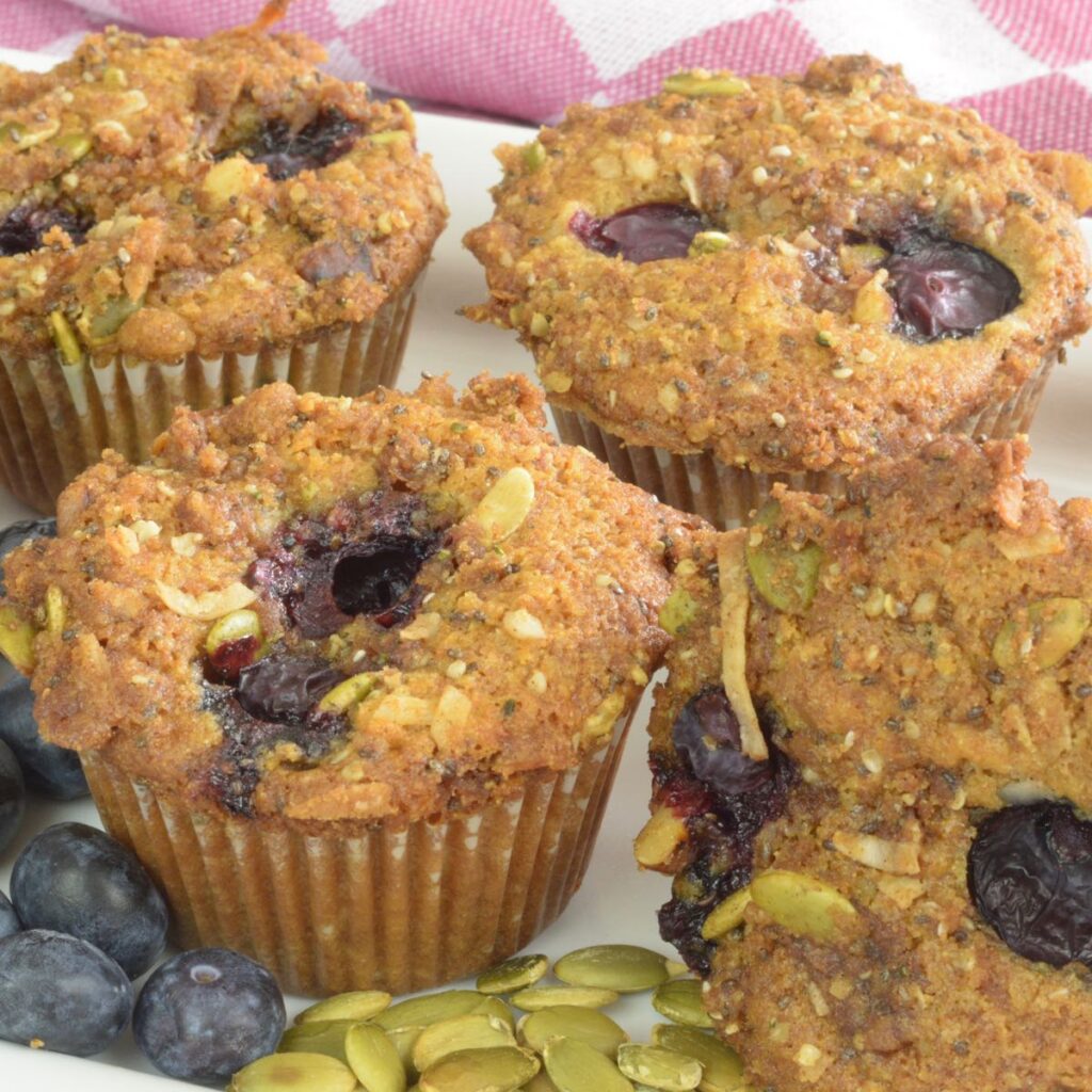 Gluten free Blueberry Muffins surrounded by fresh blueberries and pumpkin seeds.