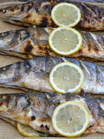 A tray of whole Grilled Branzino garnished with lemon slices.