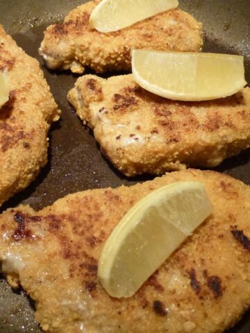 Gluten Free Breaded Pork Chops in a frying pan topped with lemon wedges.