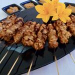 A platter with bamboo skewers of chicken satay with peanut sauce on the side.