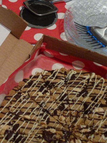 A large gluten free Chocolate Chip Cookie Pizza drizzled with white chocolate and served in a pizza box.