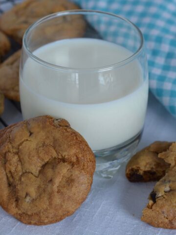 A baking rack of gluten free Chocolate Chip Cookies and a glass of milk.