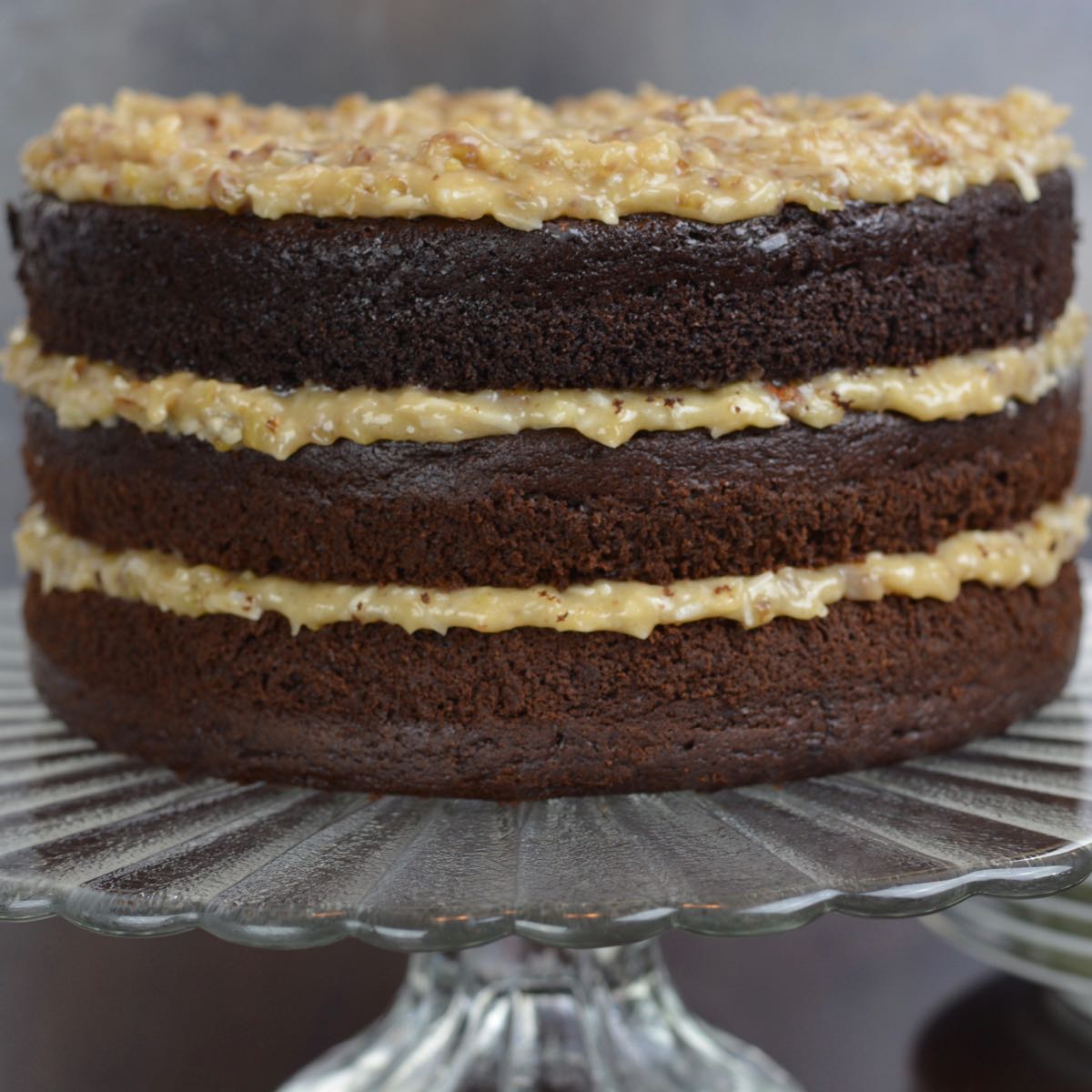 A three layer German Chocolate Cake with coconut-pecan filling on a pedestal tray.