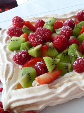 A rectangular Holiday Pavlova filled with cream and topped with strawberries, raspberries and kiwi fruit.