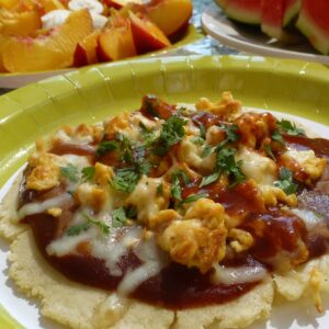 A paper plate with homemade soft corn tortillas topped with enchilada sauce, scrambled eggs and cheese, a hearty Mexican Huevos Rancheros.