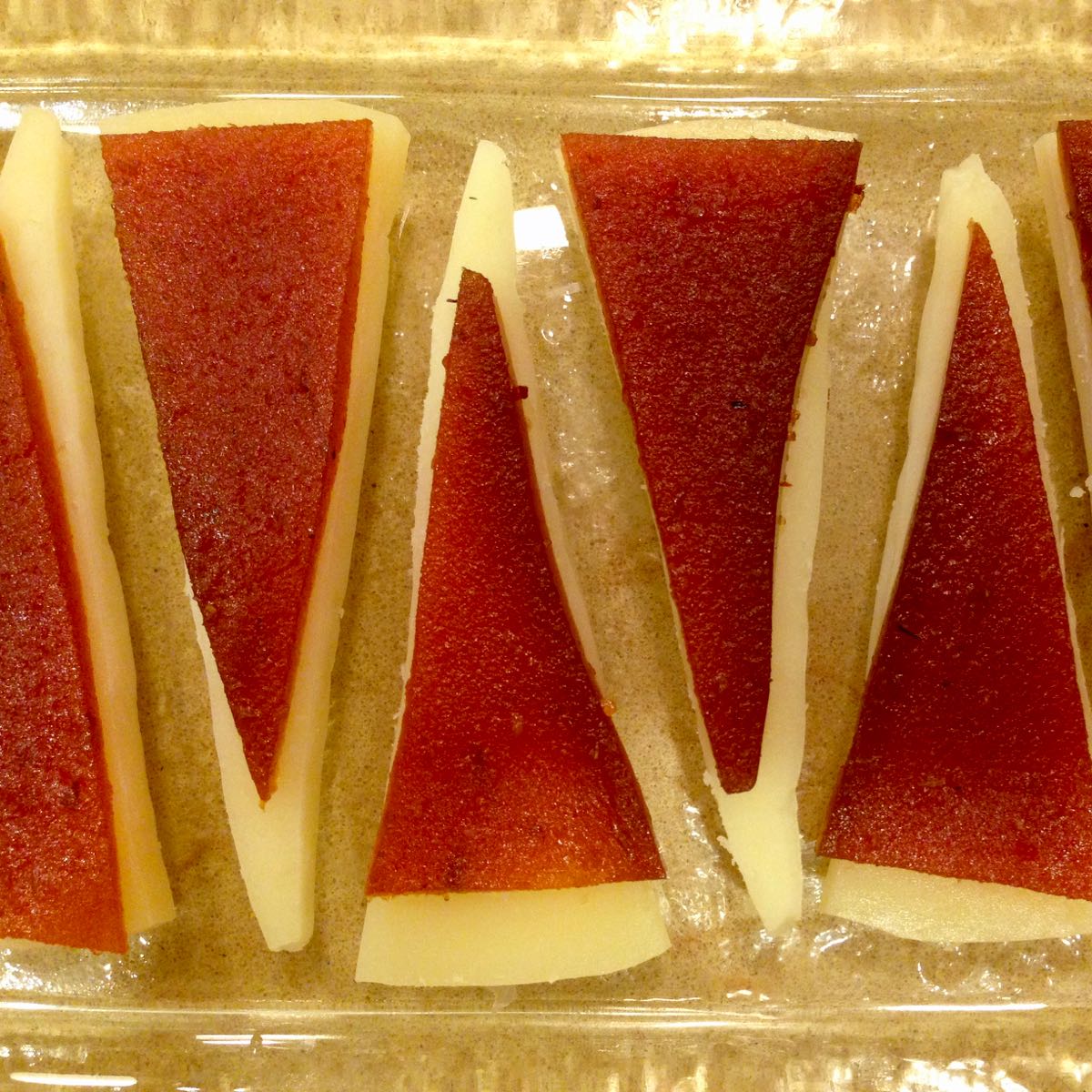 A rectangular platter with triangles of Manchego cheese covered with a slightly smaller triangle of Quince Paste.
